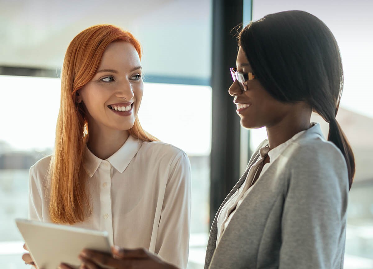Two smiling young professionals stop to compare notes